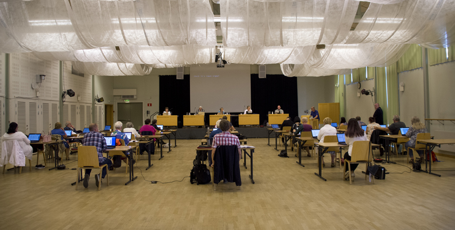 Kommunfullmäktige från ett sammanträde i Folkets hus. Fotot är taget bakifrån så att man ser ledamöterna sitta ner och längst fram syns mötespresidiet. 