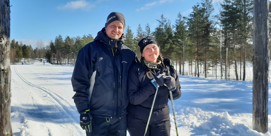 Lärarna Jesper och Marlene står tillsammans. Marlene har skidorna på sig. Bakom dem är klarblå himmel och runt dem vit snö. 