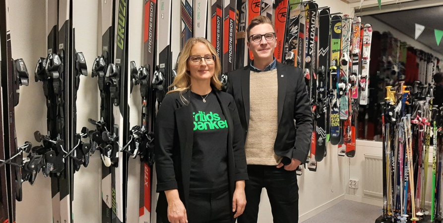 Ann-Eva Holmström och Andreas Eliasson står framför flera upphängda skidor på Fritidsbanken. 