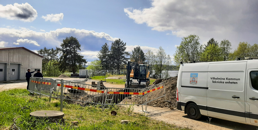 Bilden visar gaveln på reningsverket till vänster. Mitt i bild en grävmaskin som gör förberedande arbeten. I förgrunden till höger står en vit skåpbil med texten "Vilhelmina kommun. Tekniska enheten". 