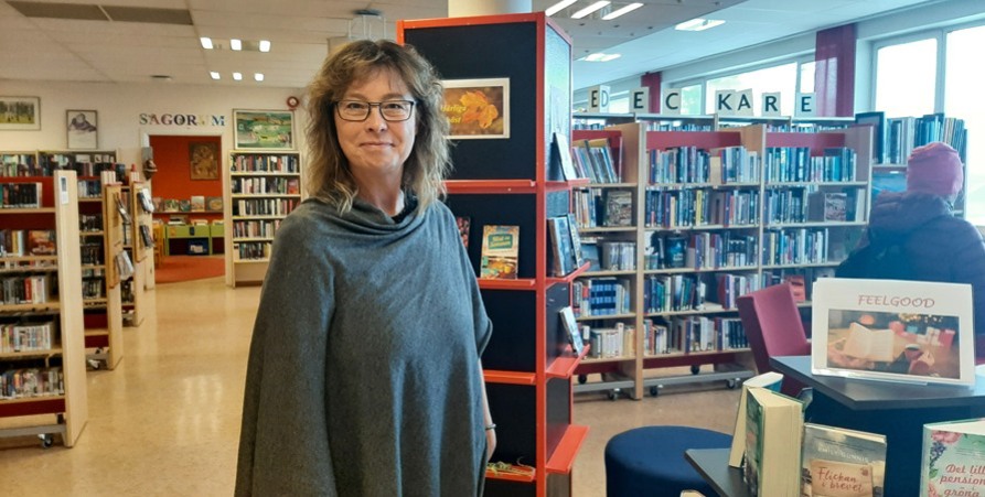 Anna står mitt i biblioteket med bokhyllor bakom sig.