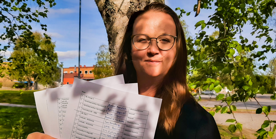 Fältsekreterare Felicia Blomqvist tittar in i kameran. Hon står under ett träd och löven skuggar delvis hennes ansikte. I handen håller hon tre pappersark. 