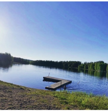 En badplats med brygga ut i en blå, stilla sjö med klarblå himmel.